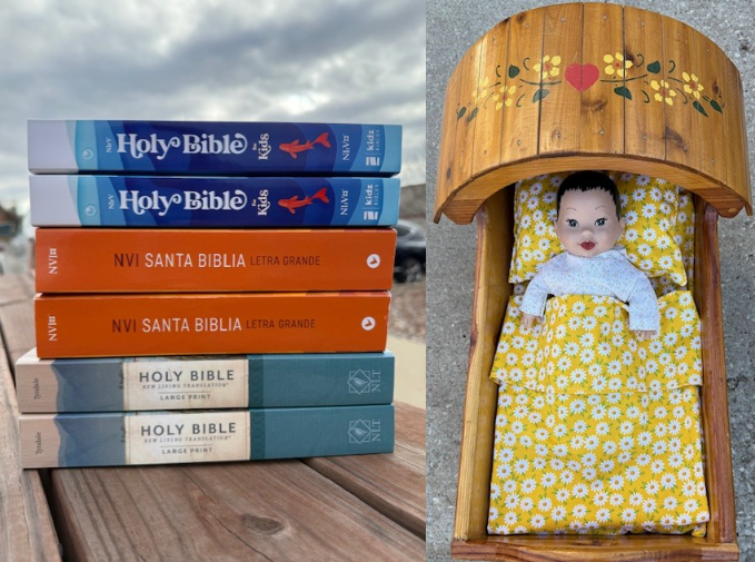 a stack of bibles on a table and a baby doll in a wooden bassinet